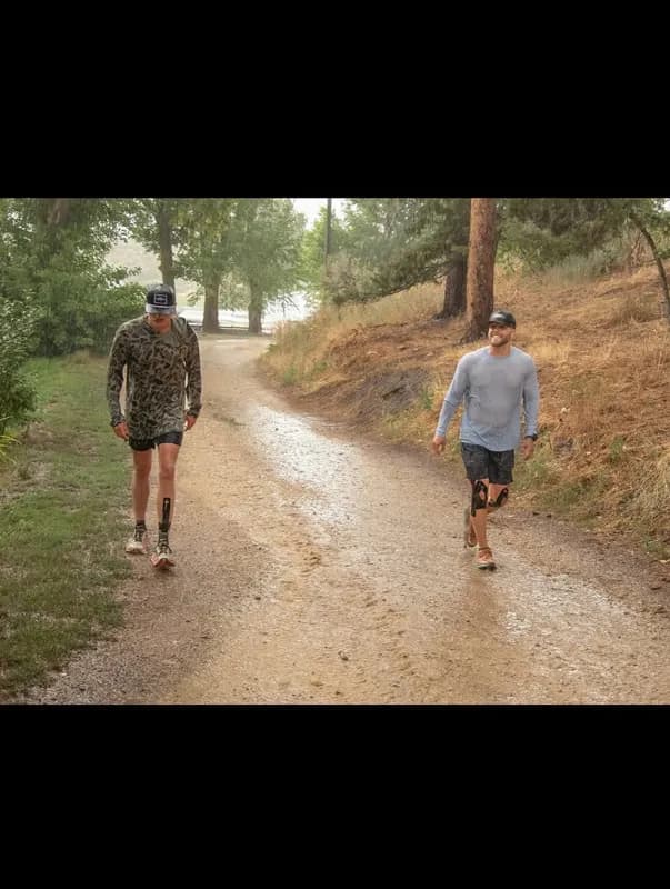 Two runners walking side by side on a tree-lined dirt trail