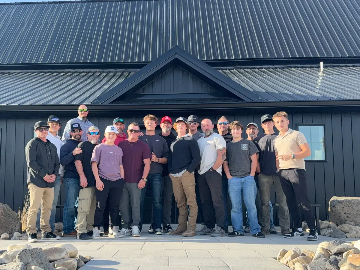 RealTalk group photo of about twenty-five men standing together outside a dark barn-style building