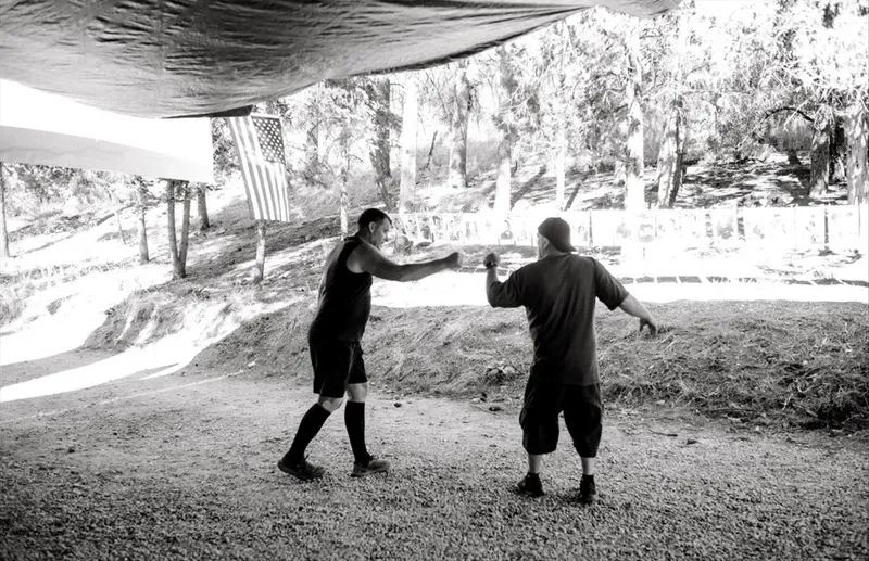 Two men sharing a fist bump under a tarp canopy with an American flag at the Last Man Standing race