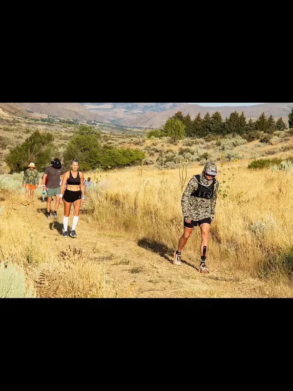 Runners hiking a golden hillside trail with Idaho mountains in the distance