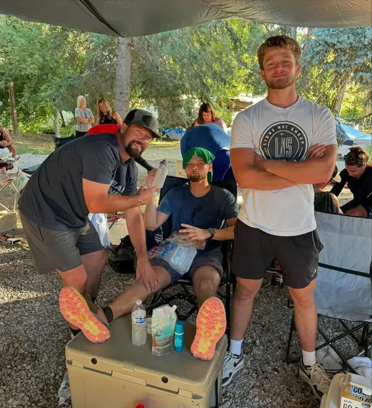 Finisher holding a wooden course plaque under the Last Man Standing banner in a Jesus Saves shirt
