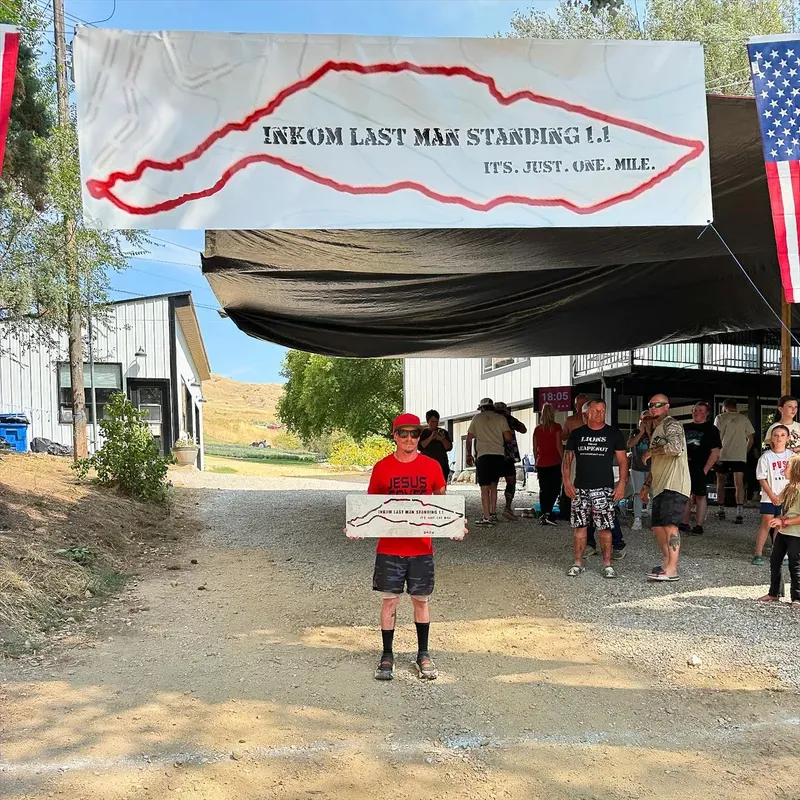 Runner in red shirt holding a finisher plaque under the Inkom Last Man Standing banner